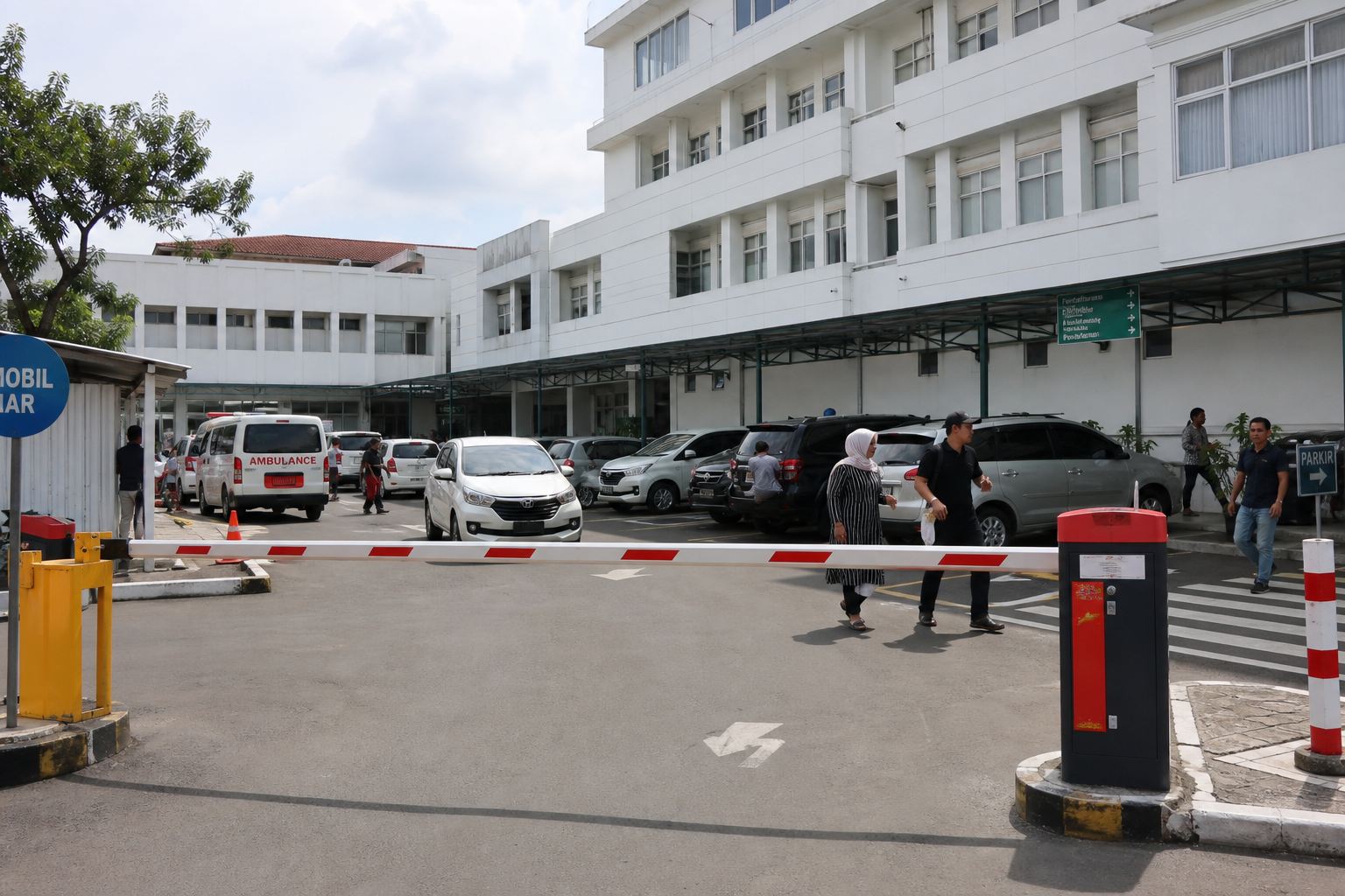Area parkir rumah sakit dengan palang dan kendaraan pengunjung