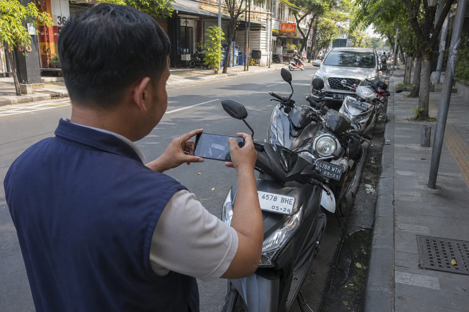 Petugas memotret plat motor yang parkir di tepi jalan
